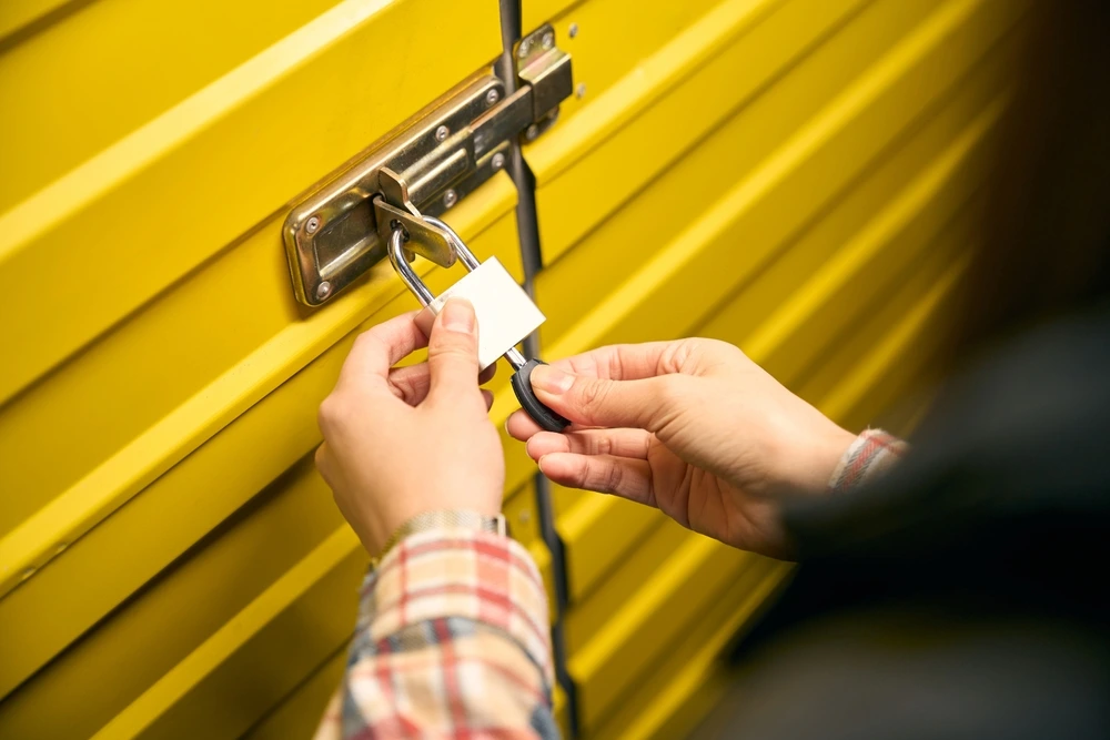 Commercial Locksmith service A person uses a key to open a heavy-duty padlock on a yellow storage unit, with security solutions provided by Rapid Locksmiths
